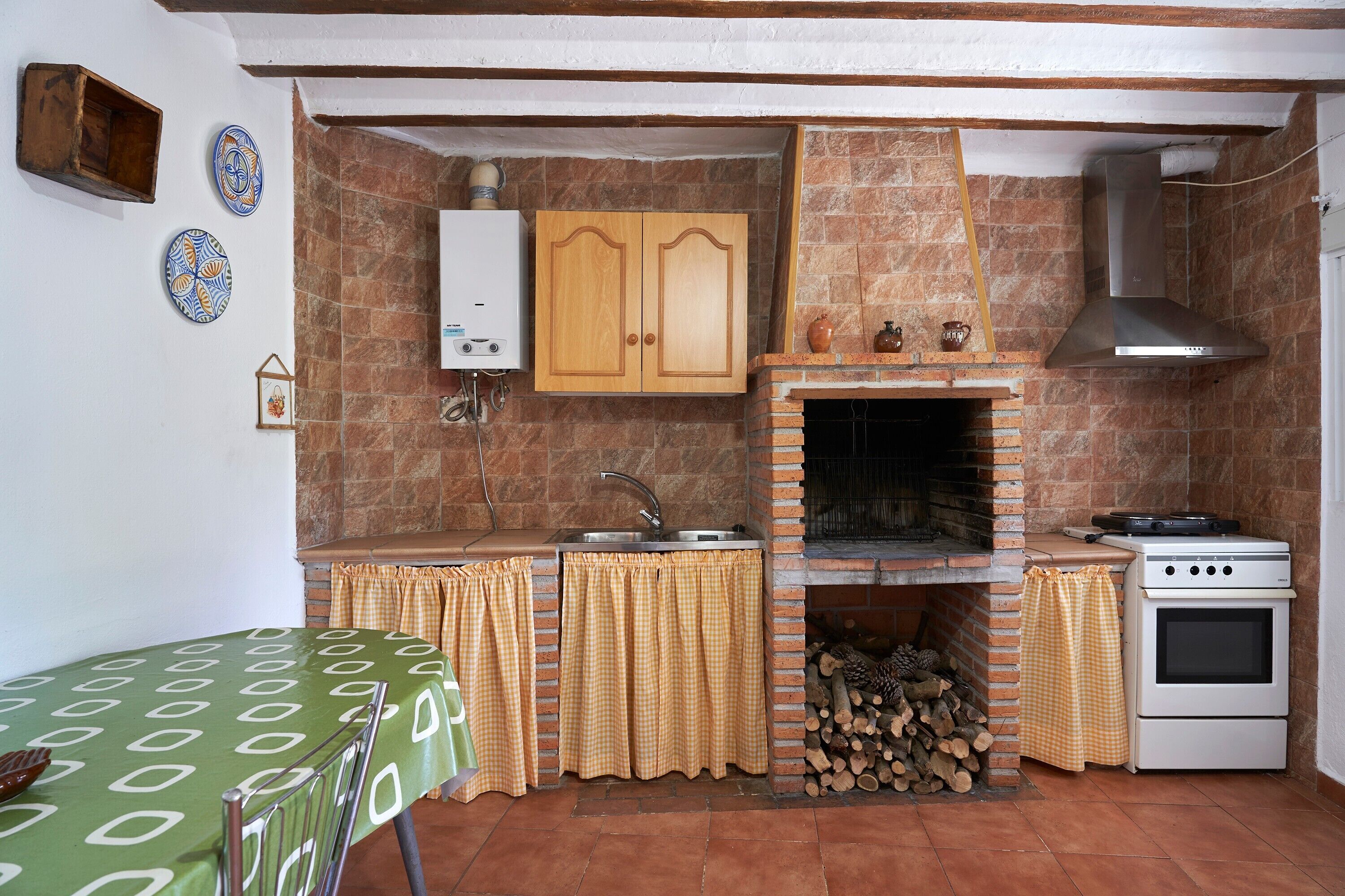 Una cocina compacta con horno integrado, un lavamanos y una estufa. Se aprecia un armario de madera sobre el lavamanos y una chimenea de ladrillo debajo.