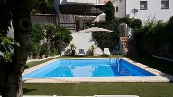 Una piscina rectangular con borde blanco, rodeada por un césped cuidado y plantas en macetas.