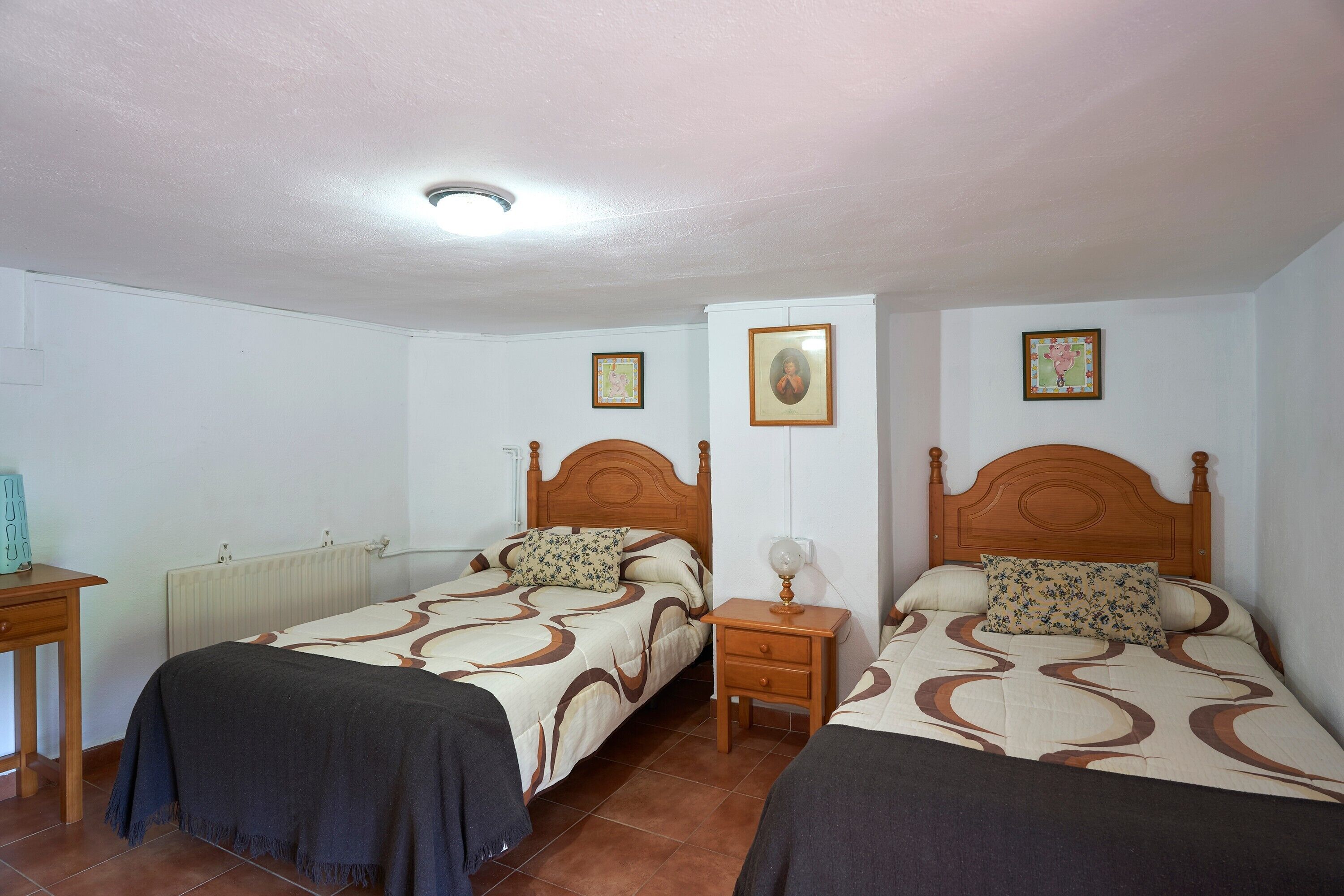 Un dormitorio con dos camas, una mesita de noche, un radiador y una lámpara en el techo.