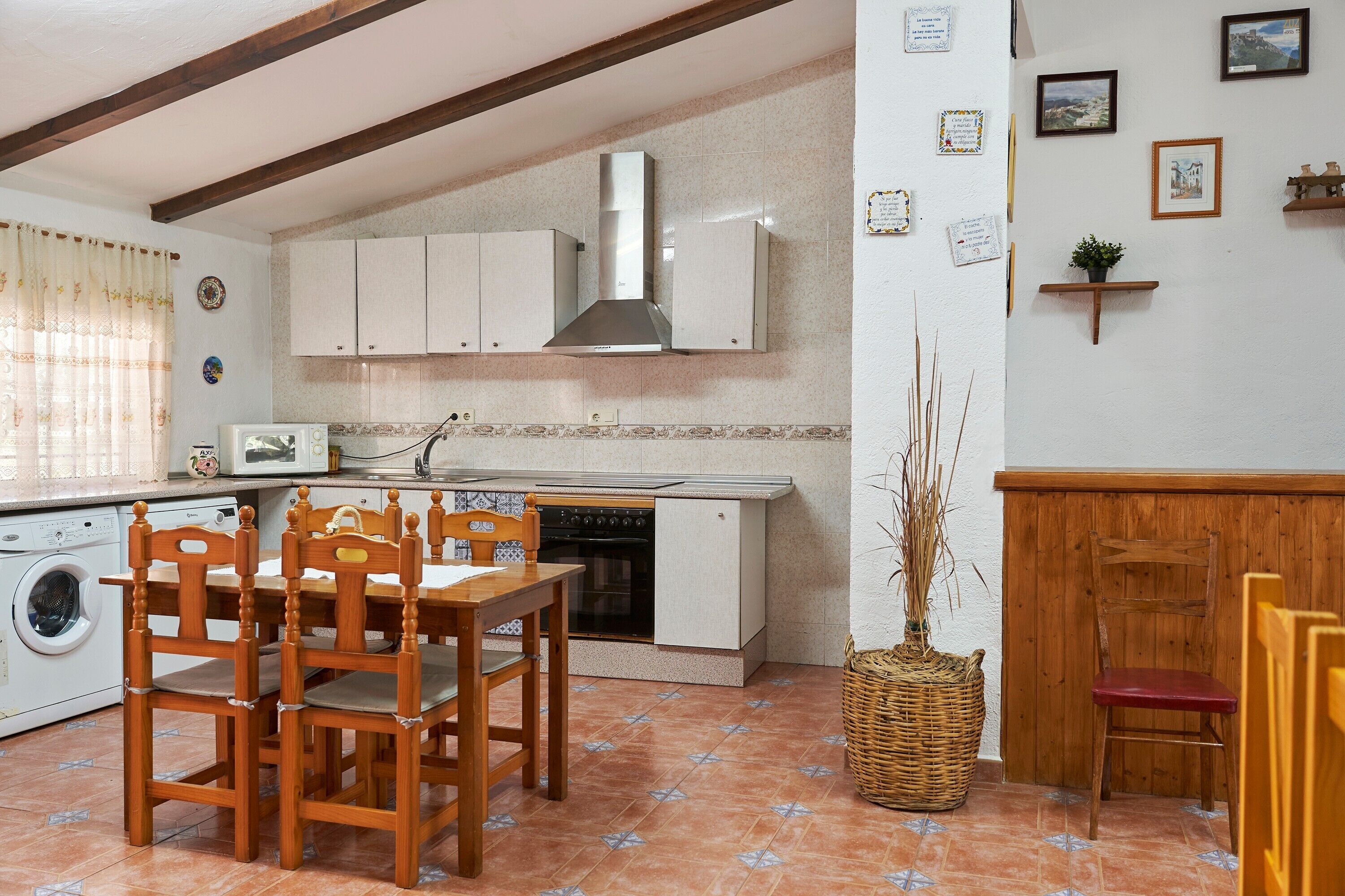 A compact kitchen with a built-in oven, a microwave, and a sink. There is a dining table with chairs and a washing machine.