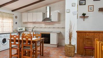 A compact kitchen with a built-in oven, a microwave, and a sink. There is a dining table with chairs and a washing machine.