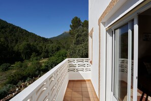 A balcony with a view of a forested hillside and a distant hilltop structure. - Holiday Home 'Alojamiento Rural Puente Honda' with Mountain View, Pool & Wi-Fi (Benatae)