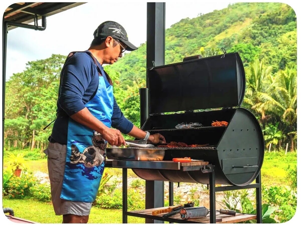 A person grilling outdoors with a view of lush greenery in the background.