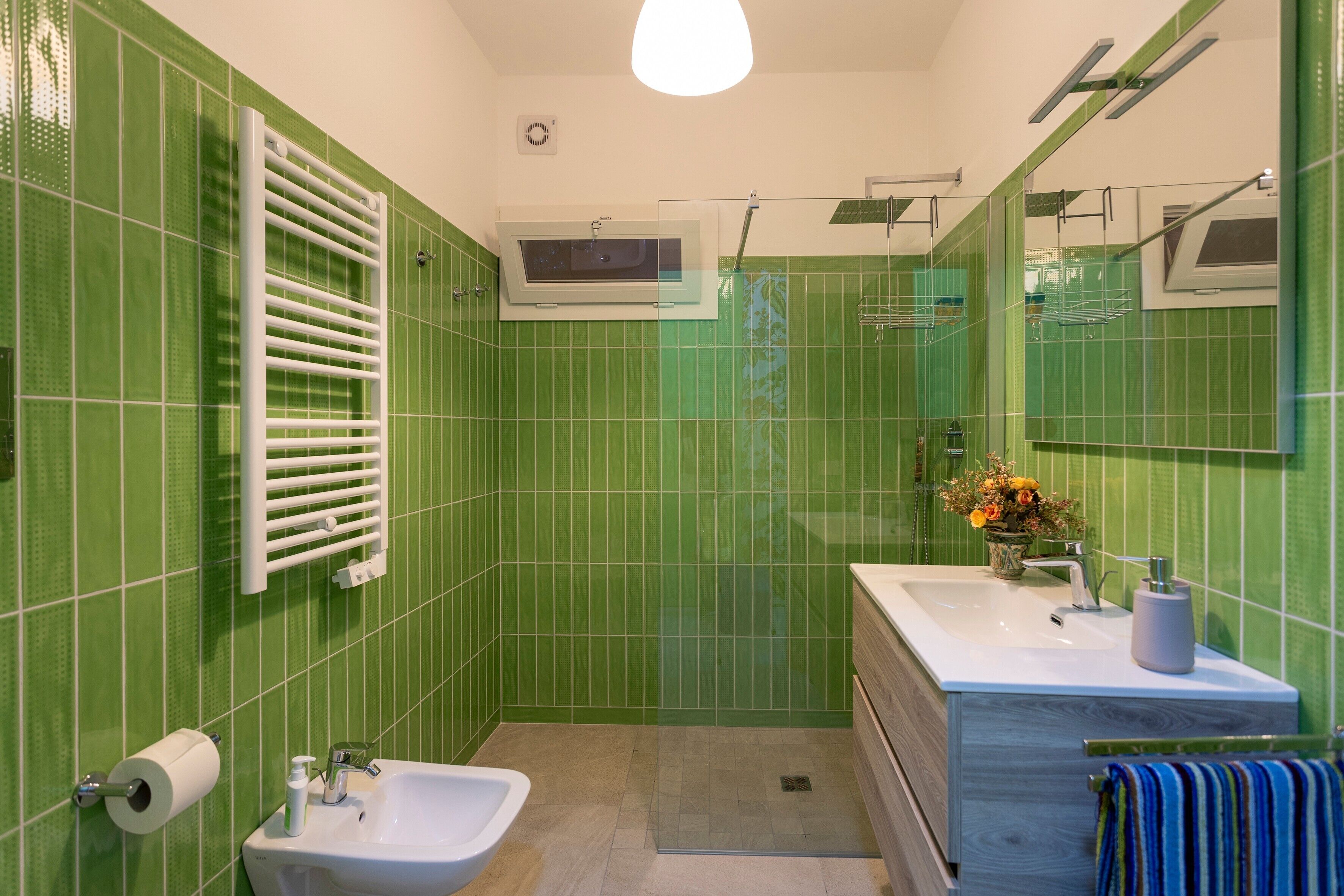 A bathroom with green tiles, a white sink, a mirror, and a shower area.