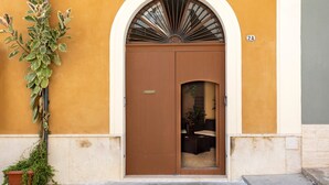 Une porte marron avec une petite fenêtre, un pot de fleurs et le numéro « 2A » peint sur le mur.