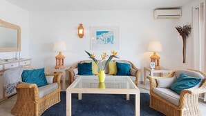 Uma sala de estar com móveis de vime, uma mesa de centro de vidro e um quadro na parede.