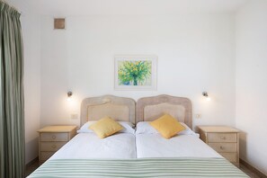 A double bed with two pillows, a bedside table, a nightstand, a wall-mounted light, and a framed picture on the wall.