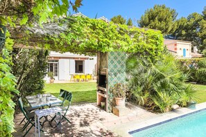 A patio with a table and chairs, a pool, and a building with a tiled wall.
