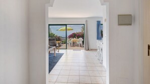 Un pasillo que conduce a un balcón con mesa y sillas, un paraguas amarillo y vistas al exterior.