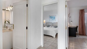 Habitación de hotel con cama, escritorio, silla, baño con lavamanos y espejo, y un cuadro en la pared.