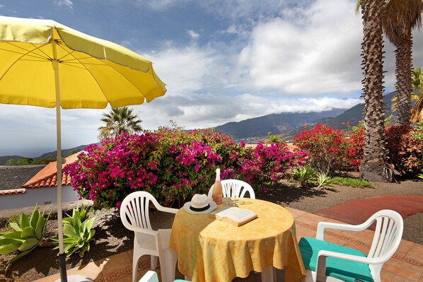 A round table with a yellow tablecloth, white chairs, and a yellow umbrella.
