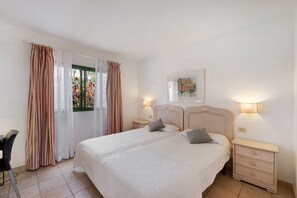A bedroom with a large bed, two bedside tables, a chair, and a window with curtains.