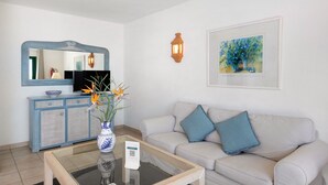 Una sala de estar con un sofá, una mesa de centro, un aparador azul, un televisor y un cuadro enmarcado.