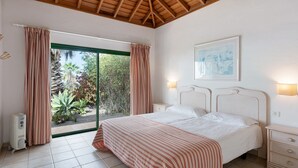 Un dormitorio con una cama, una mesita de noche, una lámpara de pared, una ventana con cortinas y vistas a zonas verdes.