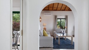 Una sala de estar con sofá, sillón, mesa de centro y vista a un espacio exterior con una silla y una mesa a través de un arco.