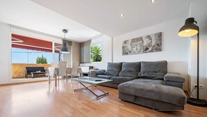 Un salon moderne avec un canapé gris, une table basse en verre et un coin repas comprenant une table et des chaises.