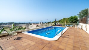 Une piscine sur le toit offrant une vue dégagée sur les gratte-ciel de la ville, entourée d’une balustrade blanche et de chaises vertes.