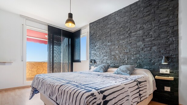 Une chambre à coucher avec un lit, un mur en pierre, une fenêtre avec des stores et un luminaire suspendu.