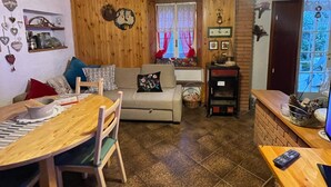 A cozy room with a wooden ceiling, a dining table with chairs, a sofa, a hanging light fixture, and a window with curtains. - Holiday Home "Casa Fiore" with Mountain View, Private Garden & Wi-Fi (Borgo Capanne)