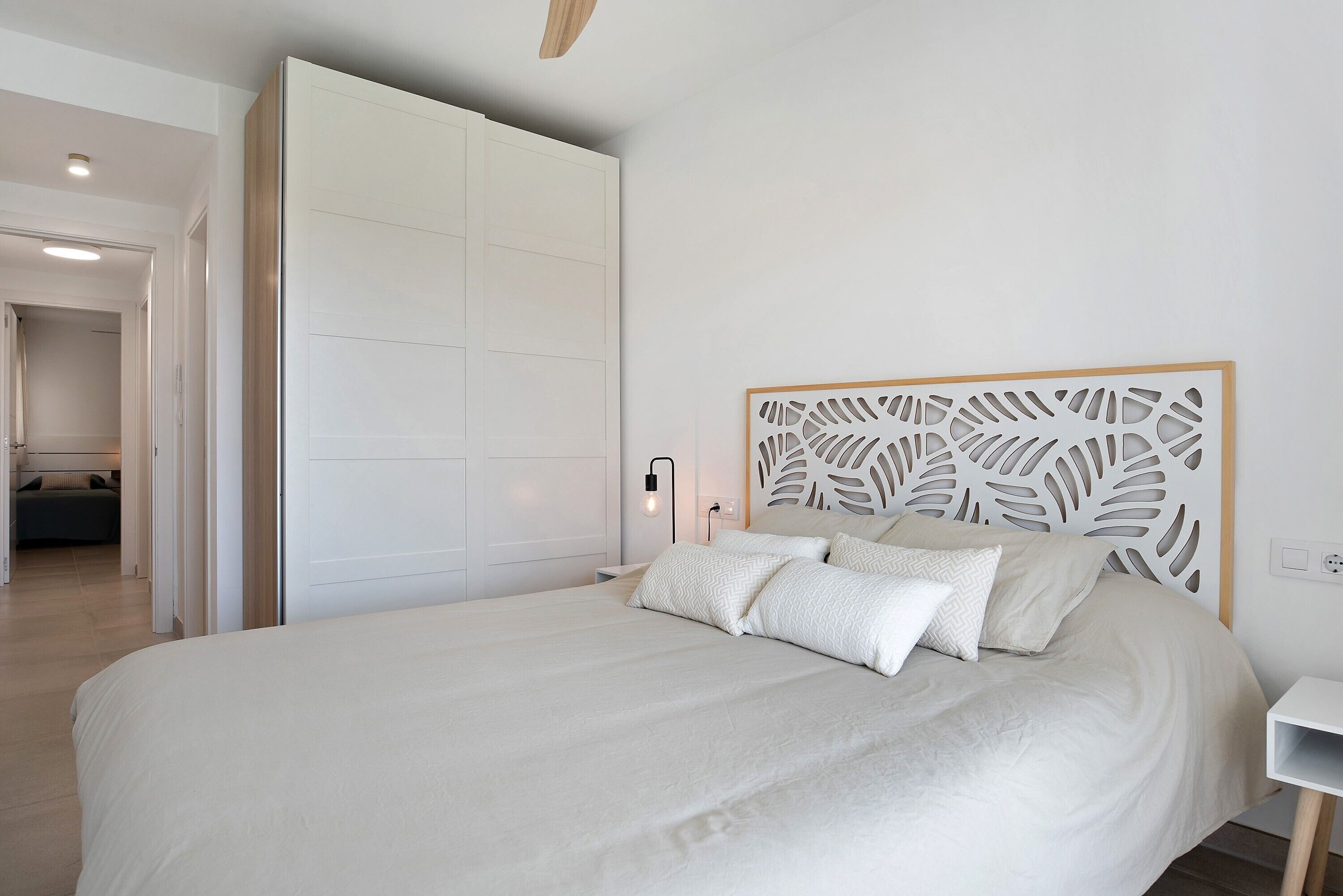 Een slaapkamer met een groot bed, een houten hoofdbord, een nachtkastje en een deur naar een andere kamer.