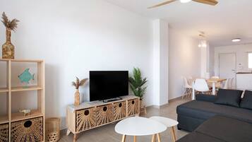 A living room with a sofa, TV, wooden shelves, and a dining area.
