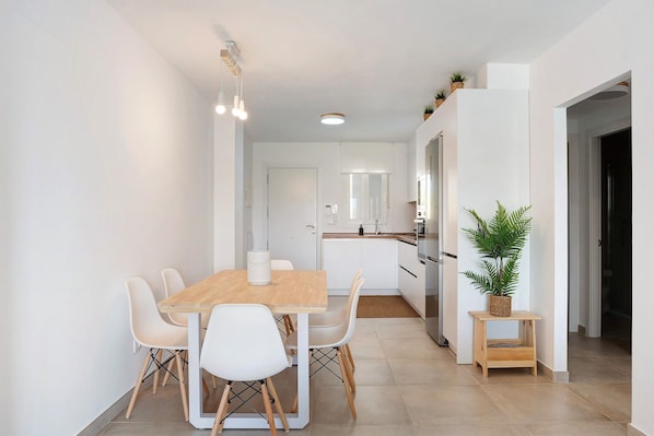A modern kitchen with white cabinets, a wooden dining table, and a potted plant.