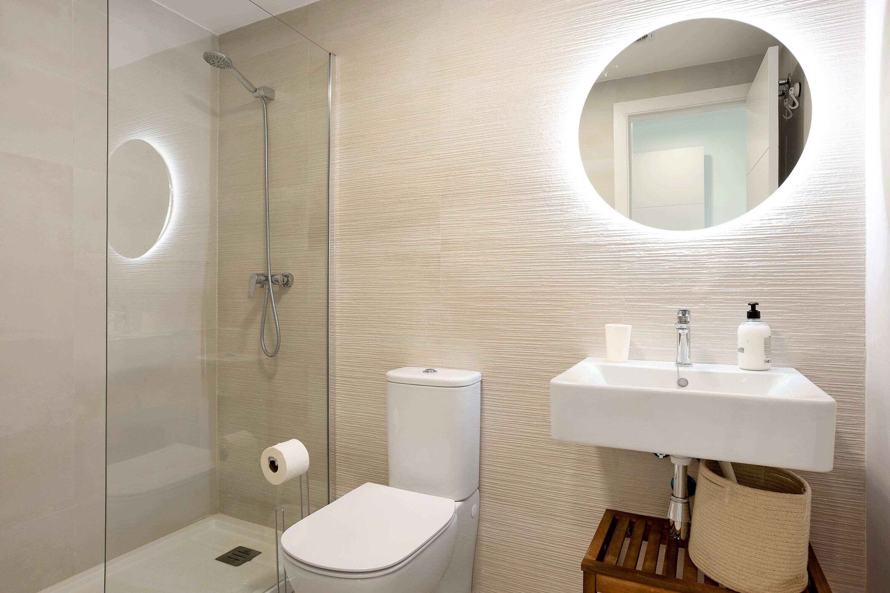 A modern bathroom with a glass-enclosed shower, a toilet, a sink with a mirror, and a small wooden stool.