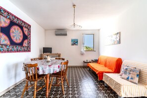 Une pièce comprenant une table à manger, des chaises, un canapé, un téléviseur et des œuvres d’art accrochées aux murs.