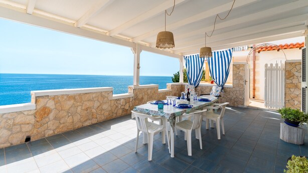 Patio esterno con tavolo apparecchiato per mangiare, pareti in pietra e vista sul mare.