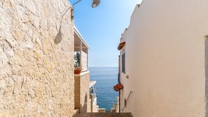 Un vicolo stretto con pareti in pietra, un lampione e vista sul mare.