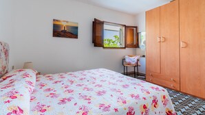 Una camera da letto con un letto, un armadio in legno, una finestra vista, un quadro appeso al muro e una sedia.