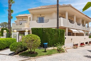 A multi-story building with a flat roof, balconies, and a well-maintained garden.