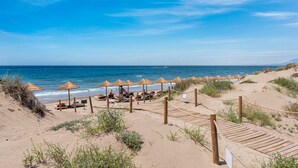 En strand med stråparasoller, træsolstole og en træpromenade.