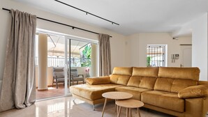 En moderne stue med en beige sofa, to små runde borde og en skydedør til et udendørs område.