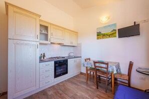 Una cocina compacta con muebles blancos, una estufa a gas, un horno y una zona de comedor con mesa y sillas.
