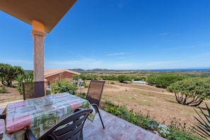 A patio with a table and chairs, overlooking a rural landscape with trees and hills.