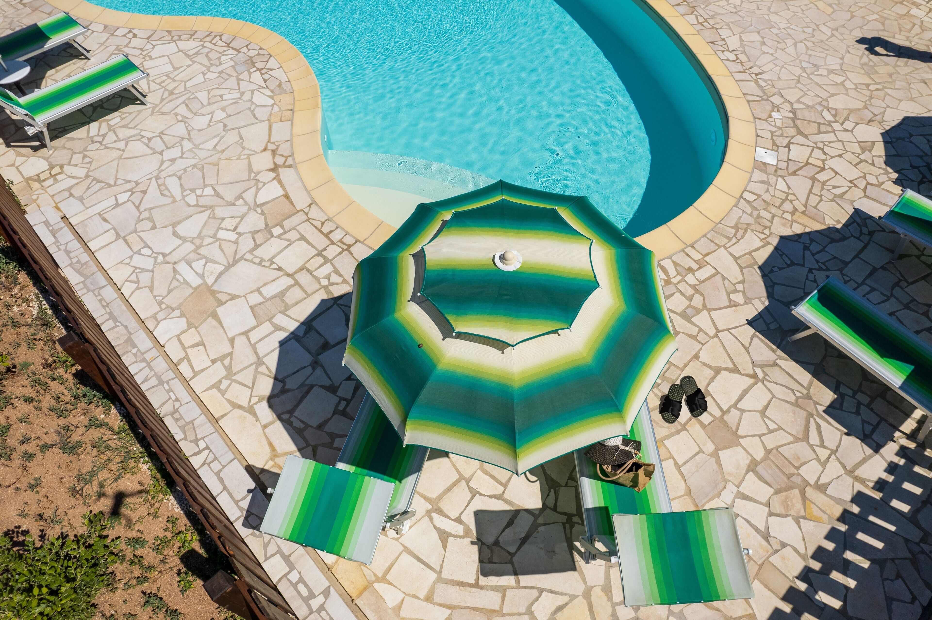 A swimming pool with a tiled deck, lounge chairs, and a green umbrella.
