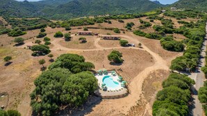 Vue aérienne d’un complexe hôtelier doté d’une piscine, entouré d’arbres et de collines.