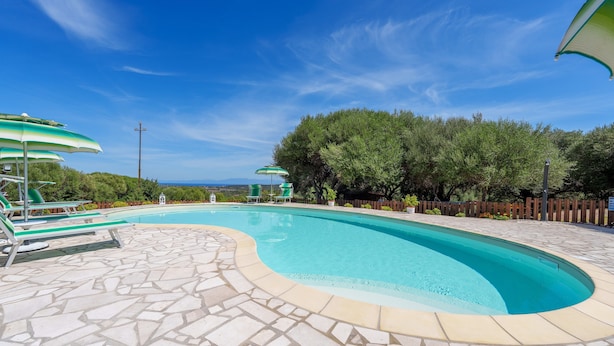 A swimming pool with a stone-tiled deck, lounge chairs, and umbrellas. - Casa Lentischio Apartment with Sea View, Shared Pool, Terrace, and Wi-Fi (Aglientu)