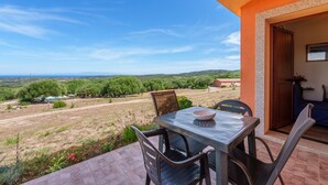 An outdoor patio with a table and chairs, a view of the countryside, and a building entrance. - Casa Lentischio Apartment with Sea View, Shared Pool, Terrace, and Wi-Fi (Aglientu)