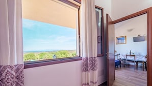 A room with a large window, a door leading to a dining area, and a flat-screen TV on the wall. - Casa Lentischio Apartment with Sea View, Shared Pool, Terrace, and Wi-Fi (Aglientu)