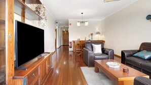 A modern living room with a flat-screen TV, leather sofas, a wooden coffee table, and a dining area with a table and chairs. - Holiday Apartment 'Fénix Garajau' with Sea View, Balcony & Wi-Fi (Caniço)