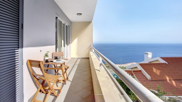 A balcony with a view of the sea, a table with chairs, and a potted plant. - Holiday Apartment 'Fénix Garajau' with Sea View, Balcony & Wi-Fi (Caniço)