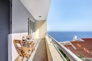 Uma varanda com vista para o mar, uma mesa com cadeiras e um vaso de planta.