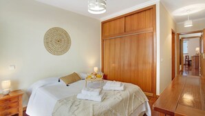 A bedroom with a bed, wooden wardrobe, bedside tables, and a wall decoration. - Holiday Apartment 'Fénix Garajau' with Sea View, Balcony & Wi-Fi (Caniço)