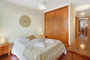Quarto com cama, guarda-roupa de madeira, mesas de cabeceira e um adorno na parede.