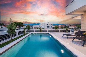 A swimming pool with a view of modern buildings and mountains in the background. - Apartment Sun Private Pool and Jacuzzi  (Novalja)