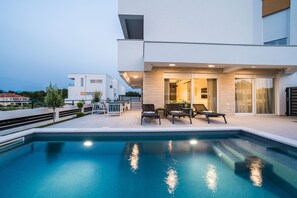 A modern pool area with a clear pool, lounge chairs, and a building with a glass door entrance. - Apartment Sun Private Pool and Jacuzzi  (Novalja)