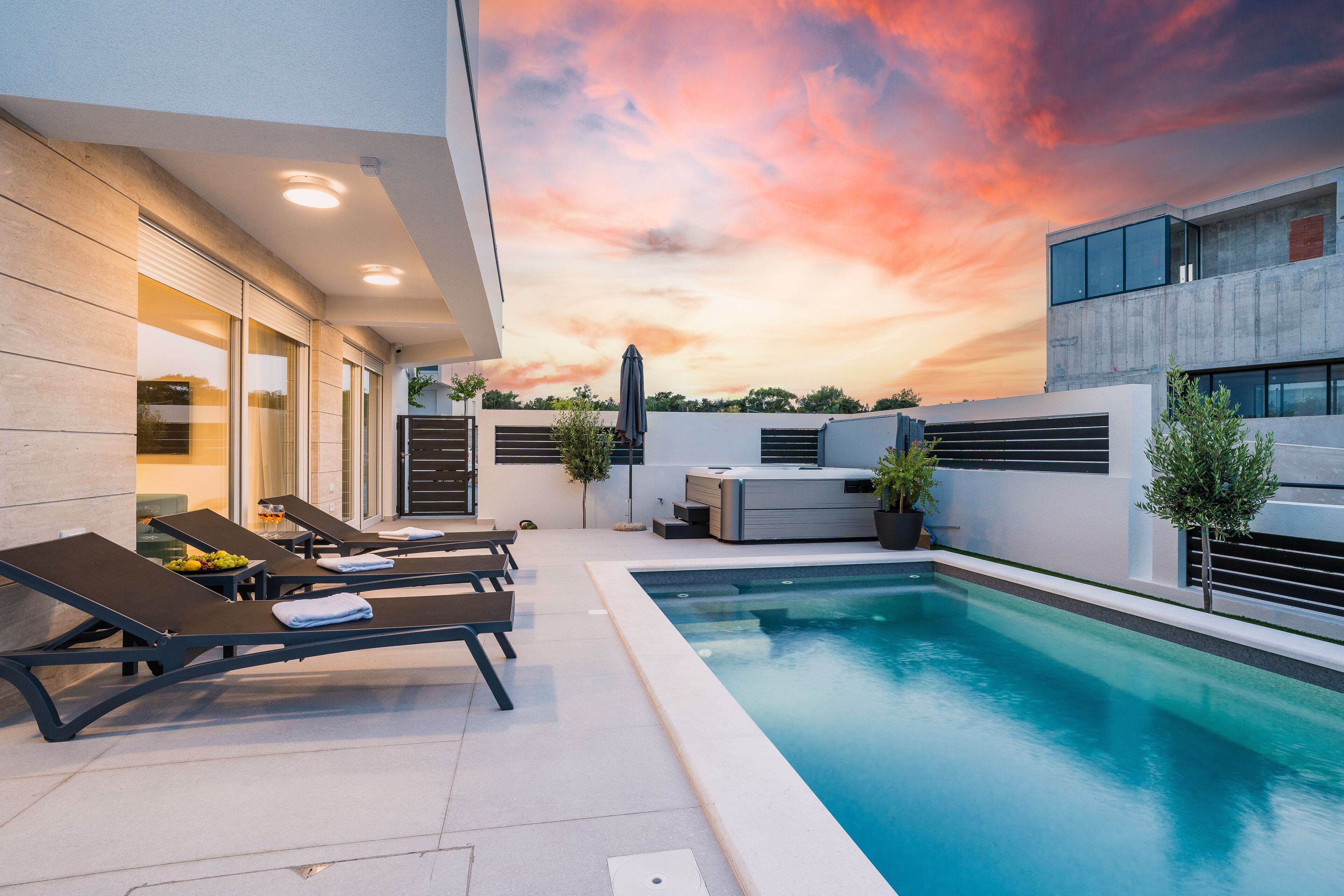 Ein moderner Poolbereich im Freien mit Liegestühlen, einem Whirlpool und Blick auf den Sonnenuntergang.