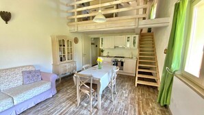 Una cocina acogedora con vigas de madera, una mesa de comedor con sillas, un sofá y una escalera.